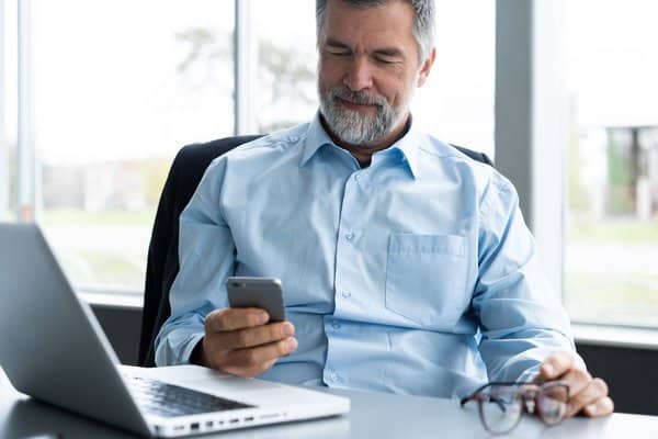 Businessman reading a text message on his phone at his desk, illustrating text message contract formation