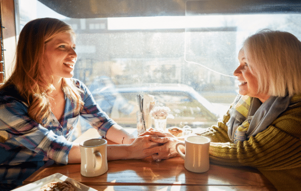 two woman sitting across table holding hands